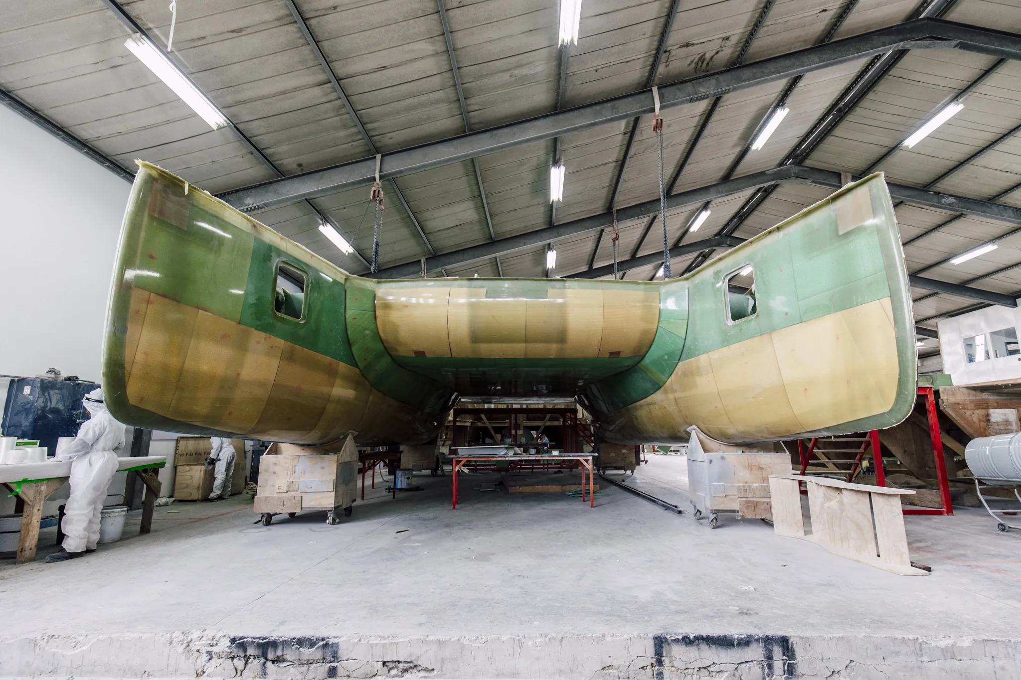 The same hull as raw resin-infused laminate, hanging on chains in the build shed