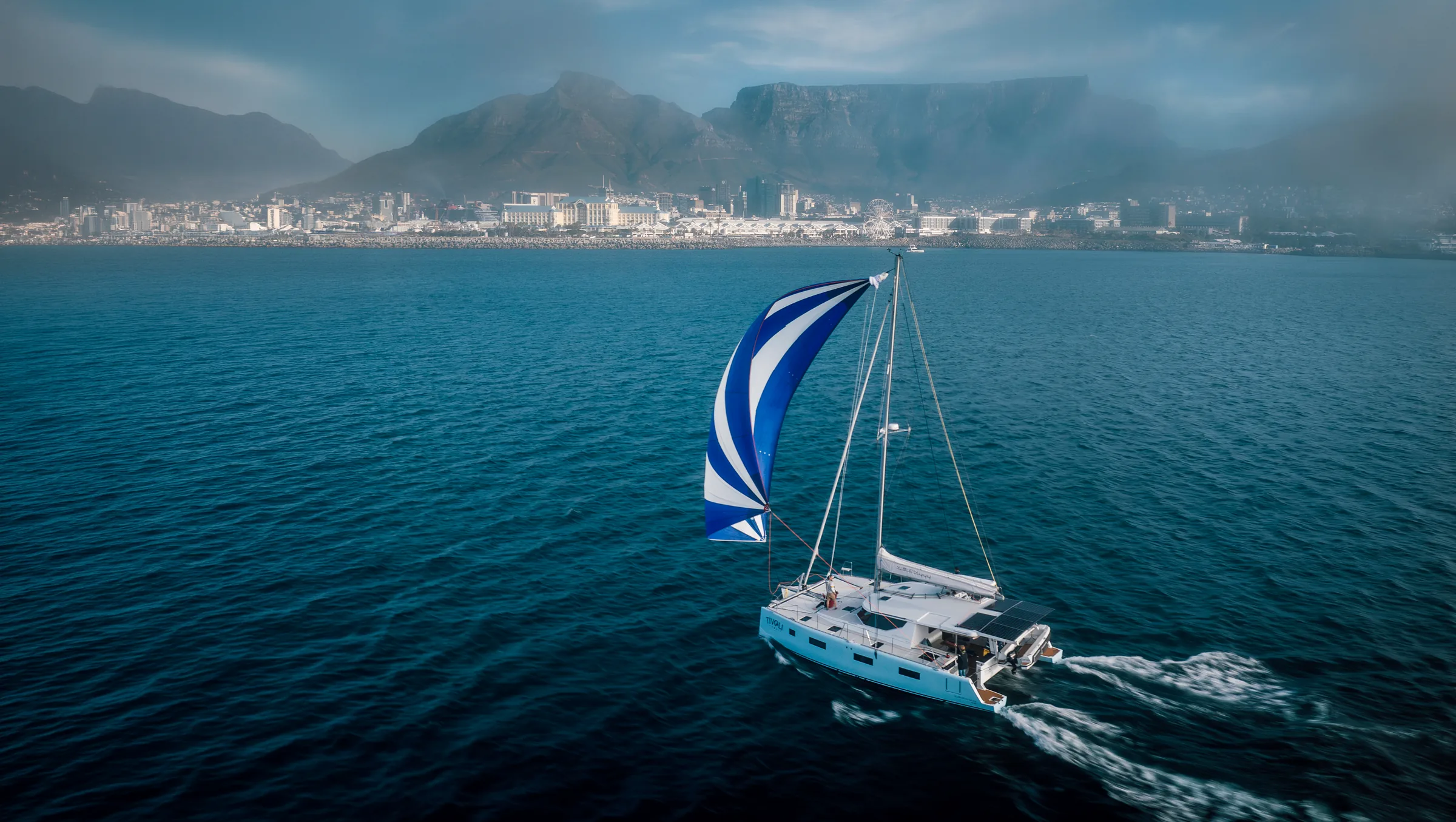 Tivoli, a Vision catamaran, under a blue and white spinnaker off Cape Town with Table Mountain behind